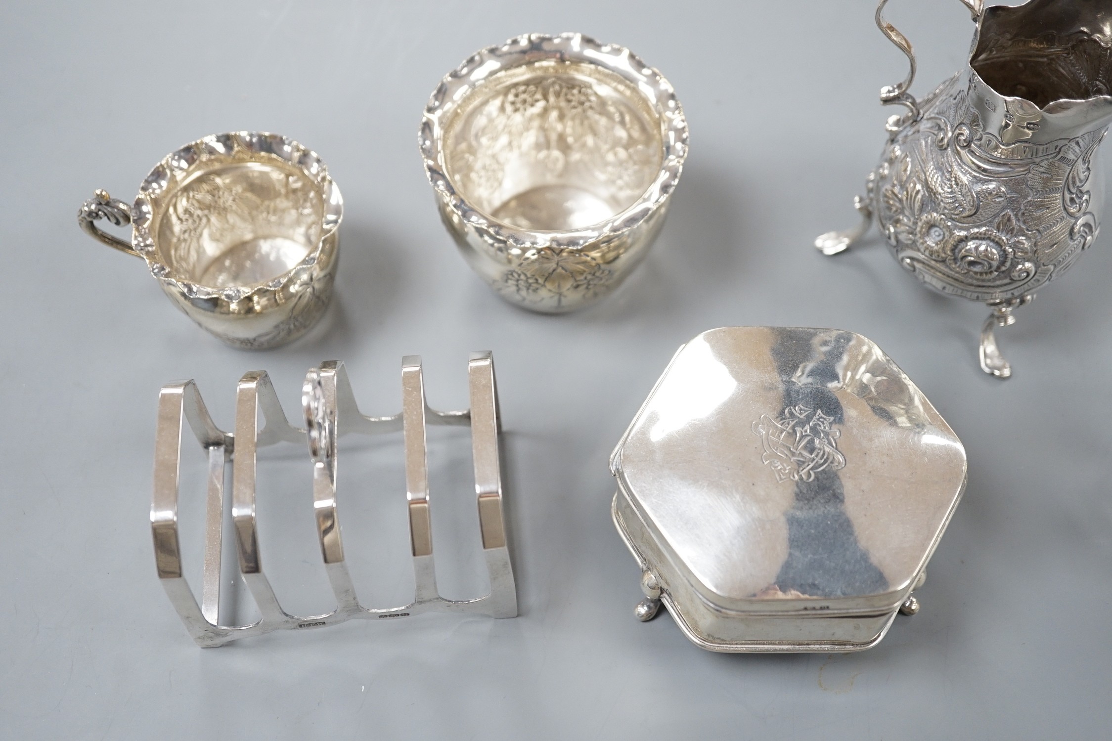 An Edwardian repousse silver bachelors cream jug and sugar bowl, Birmingham, 1904, two other late 19th/early 20th century silver cream jugs, a silver five bar toastrack and a silver mounted trinket box.